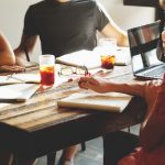 People meeting around a table with laptops, notebooks, iced tea, and iced coffee